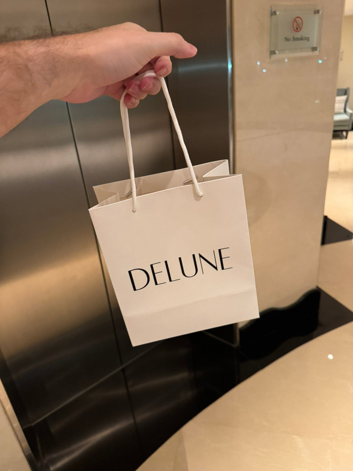 En hånd med en hvid Delune-gavepose på vej ud med en ordre
