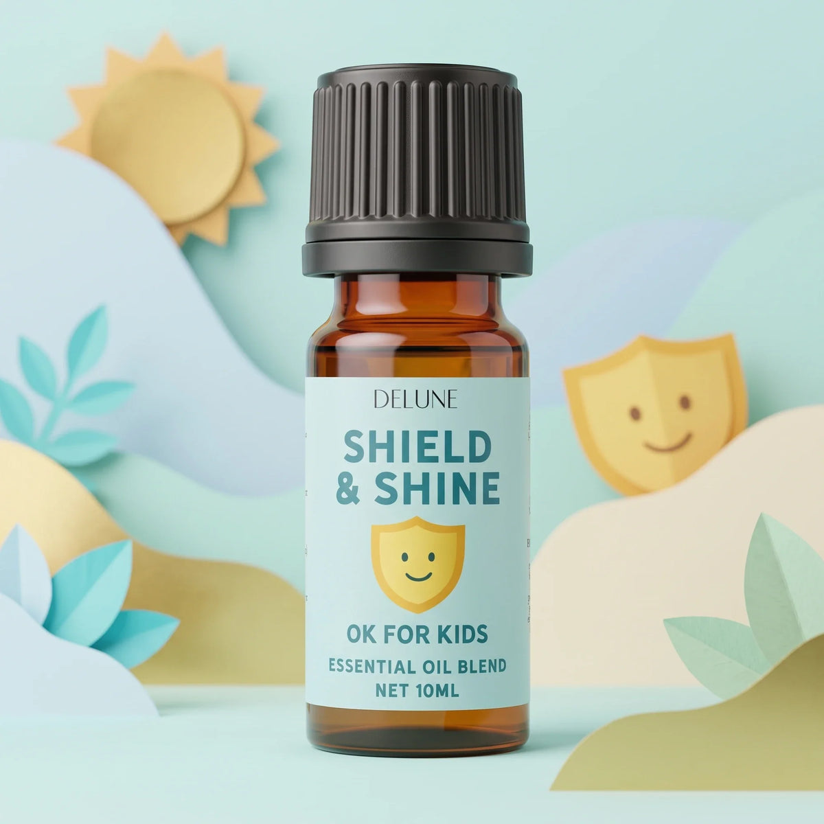 Shield & Shine (OK for Kids) – blanding af æteriske olier fra Delune i 10 ml ravfarvet flaske i en solrig, turkis papirverden med et smilende papirskjold