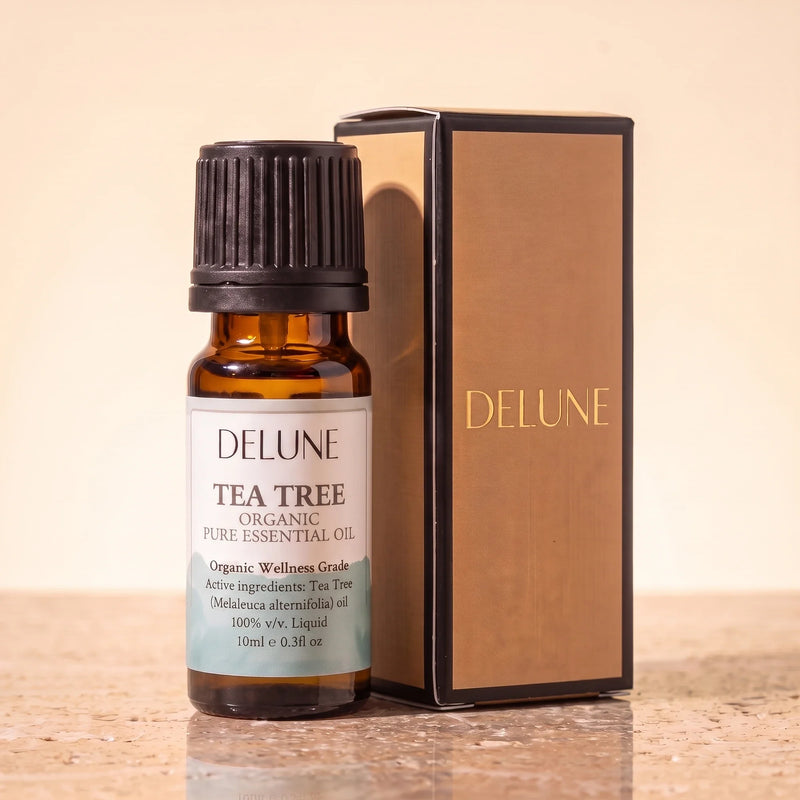 Tea tree – Organic Wellness Grade æterisk olie fra Delune i 10 ml ravfarvet glasflaske med gaveæske i guldfolie på varm travertin